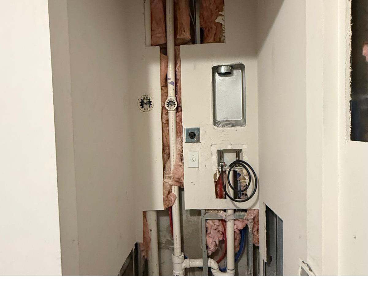 Laundry closet opened up with exposed plumbing and insulation